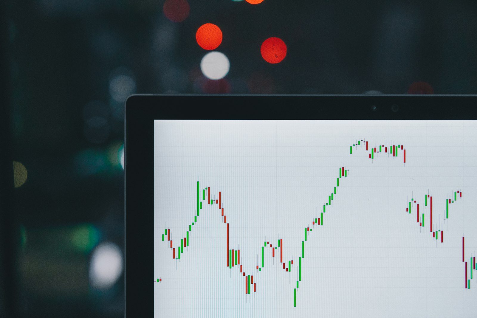 Multiple financial line charts and candlestick graphs on monitors with red and green data series